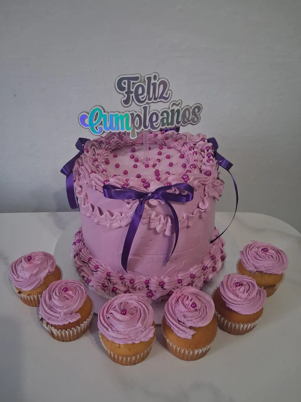 Torta rosada con letras grandes y ponquesitos decorados para celebración en Caracas